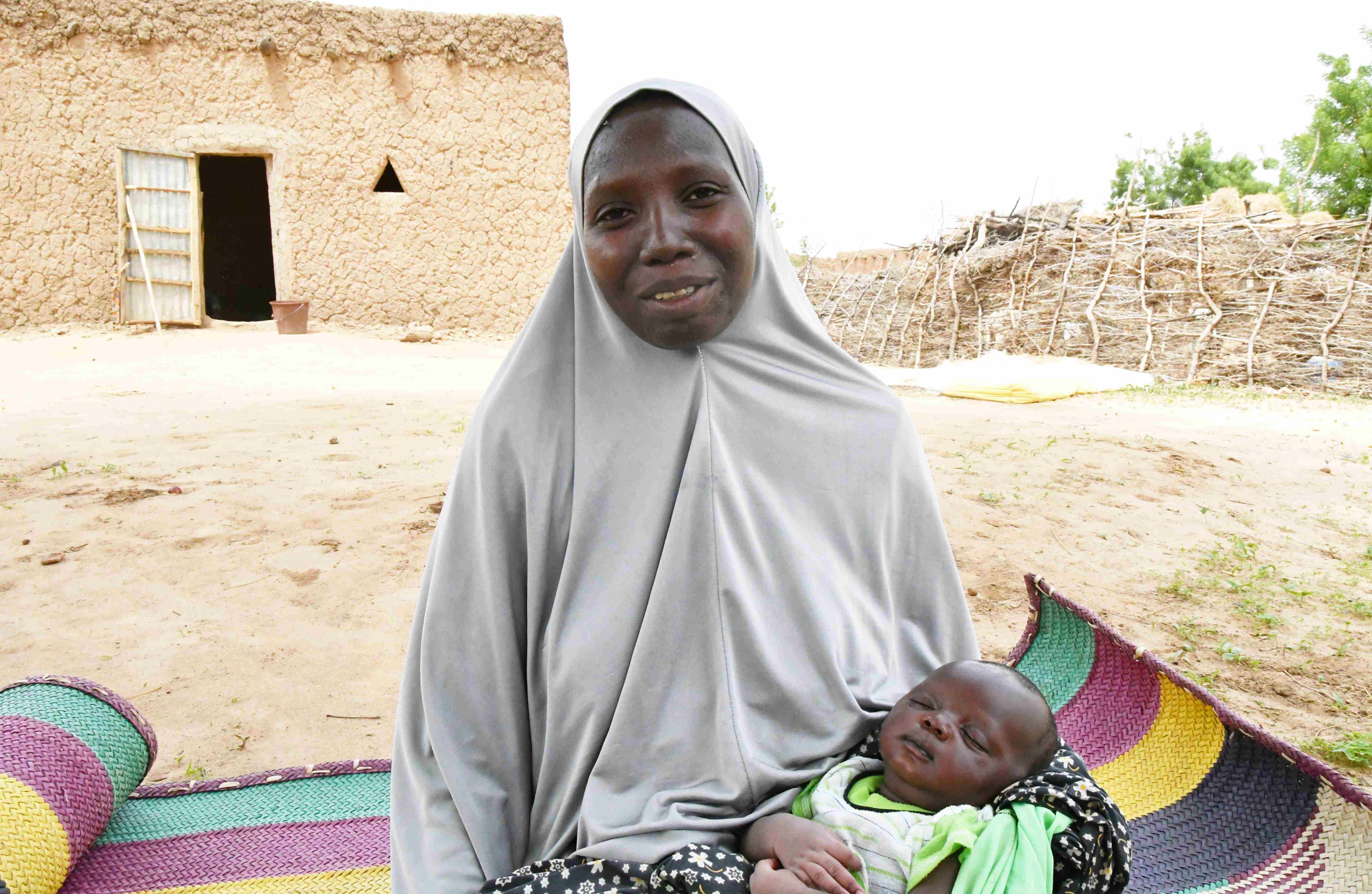 Woman in Niger sits on a mat outside, holding baby in her arms