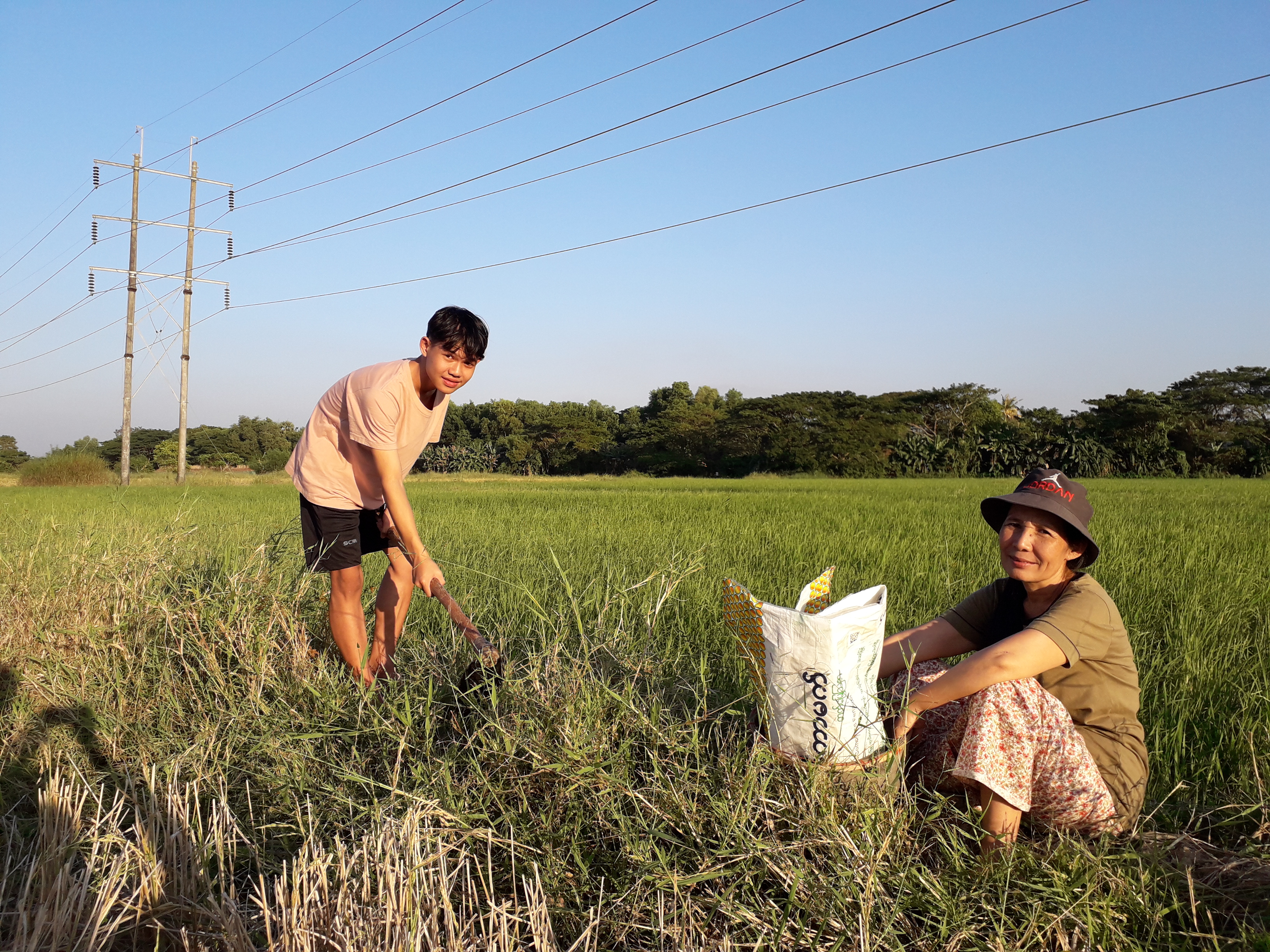 Boy from Myanmar digging in a field, his mother sat on the floor next to him