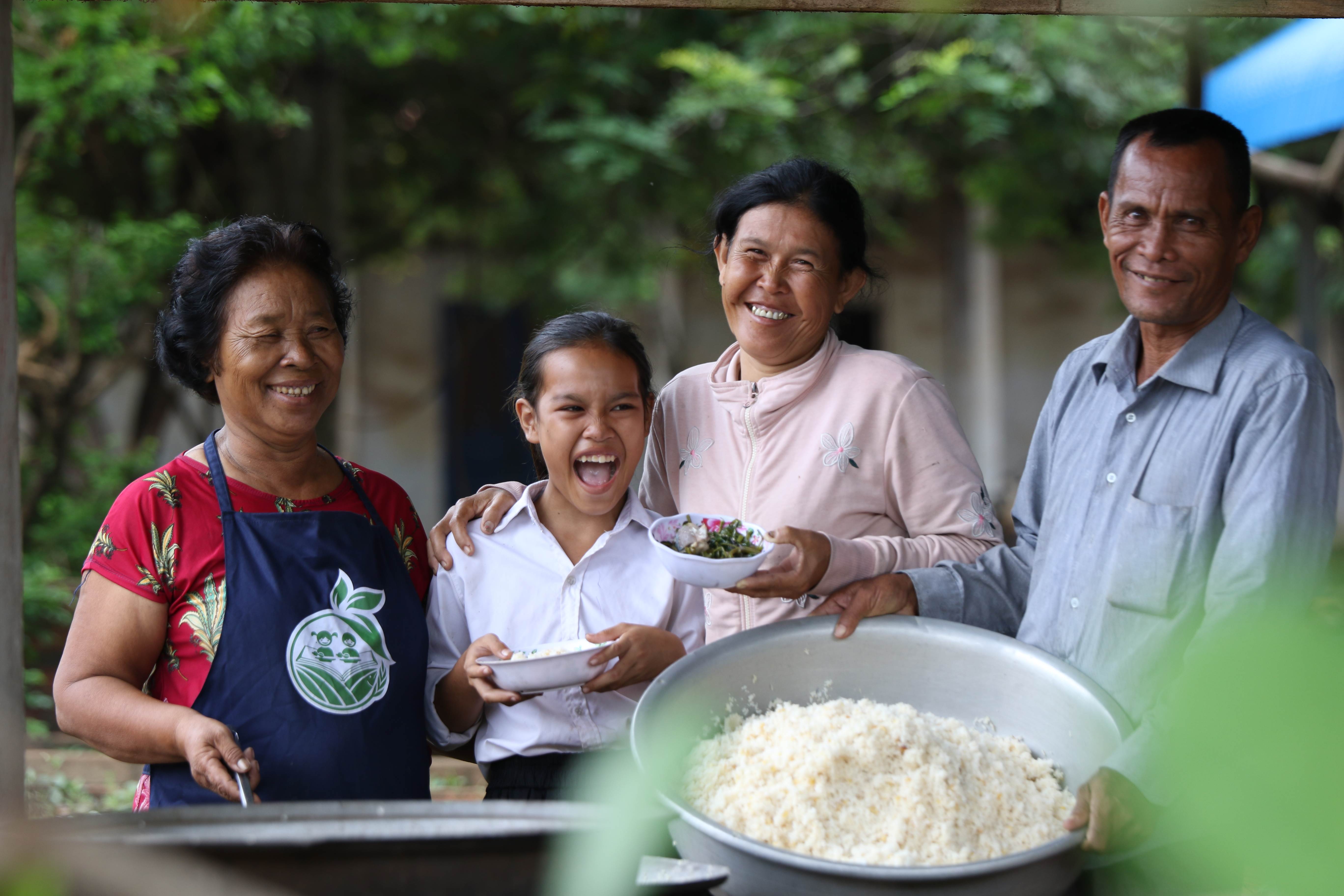 A girl smiles at the camera as she gets her free school breakfast from volunteers at her school in Cambodia