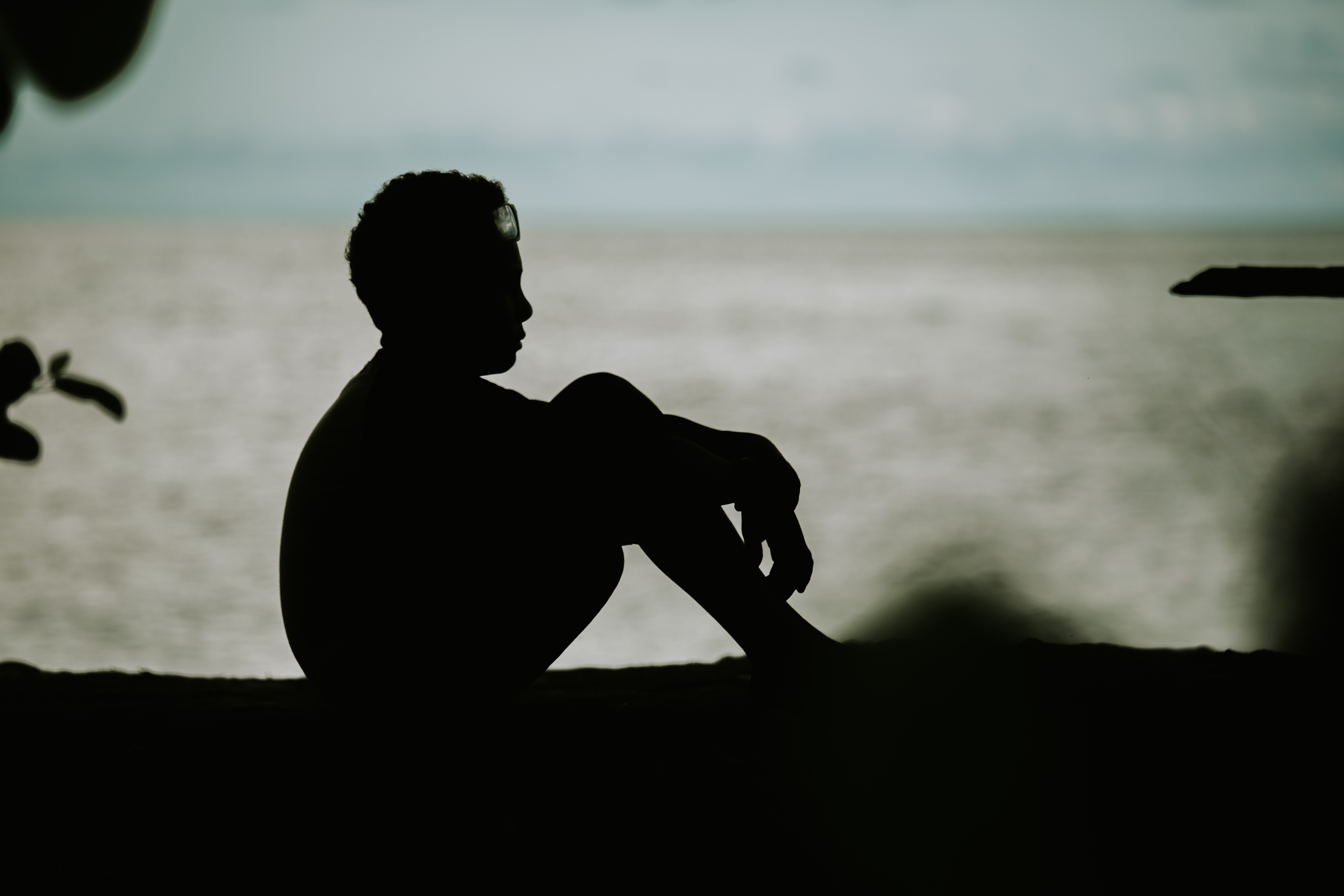 Silhouette of a boy sitting on the beach at dusk, sea in the background
