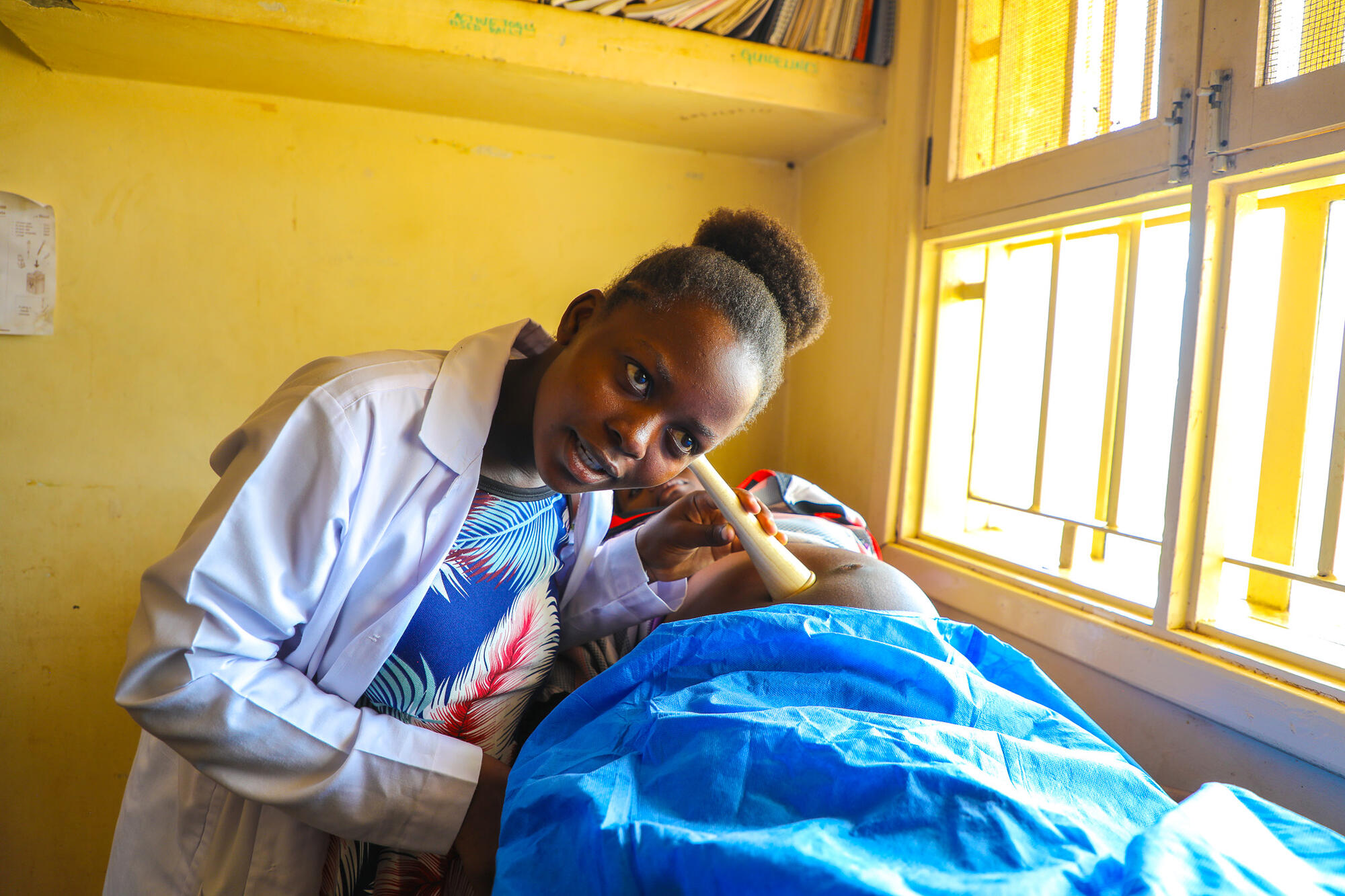 A former sponsored child, now midwife, listens to a pregnant mother's stomach