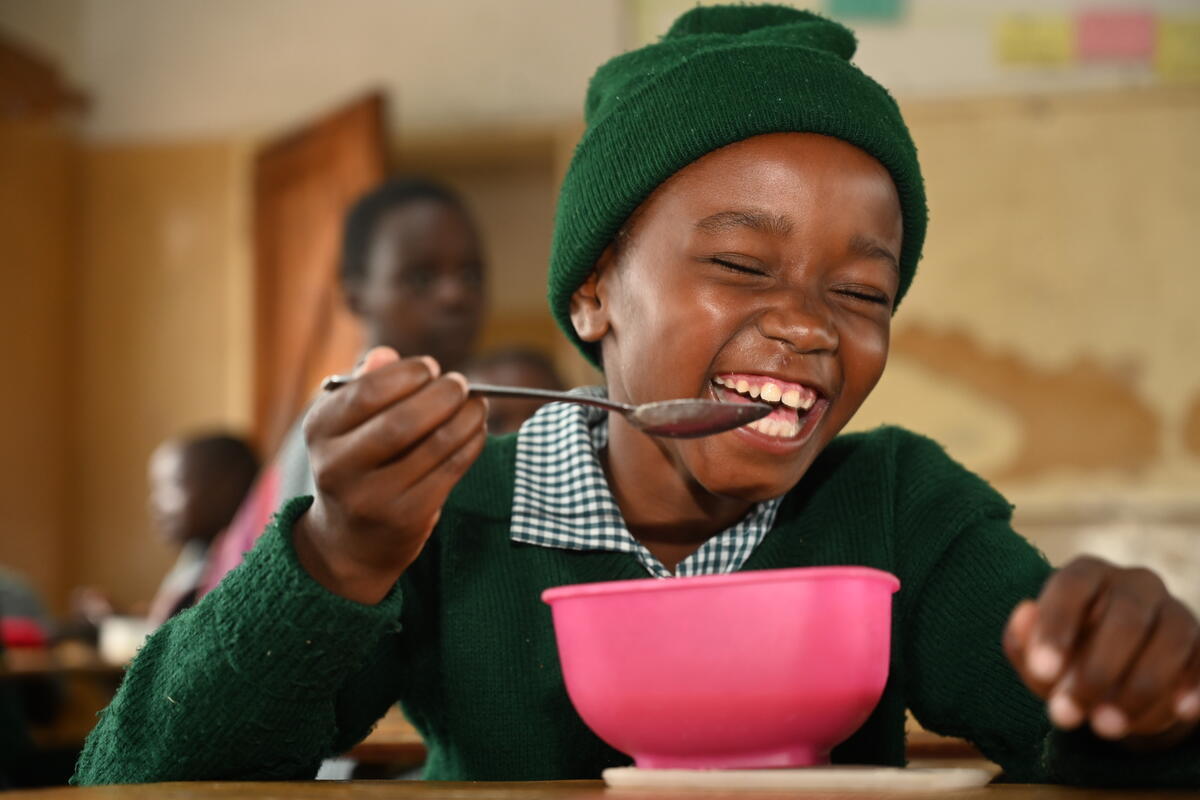 Child from Zambia beams as they sit with a bowl of food at school