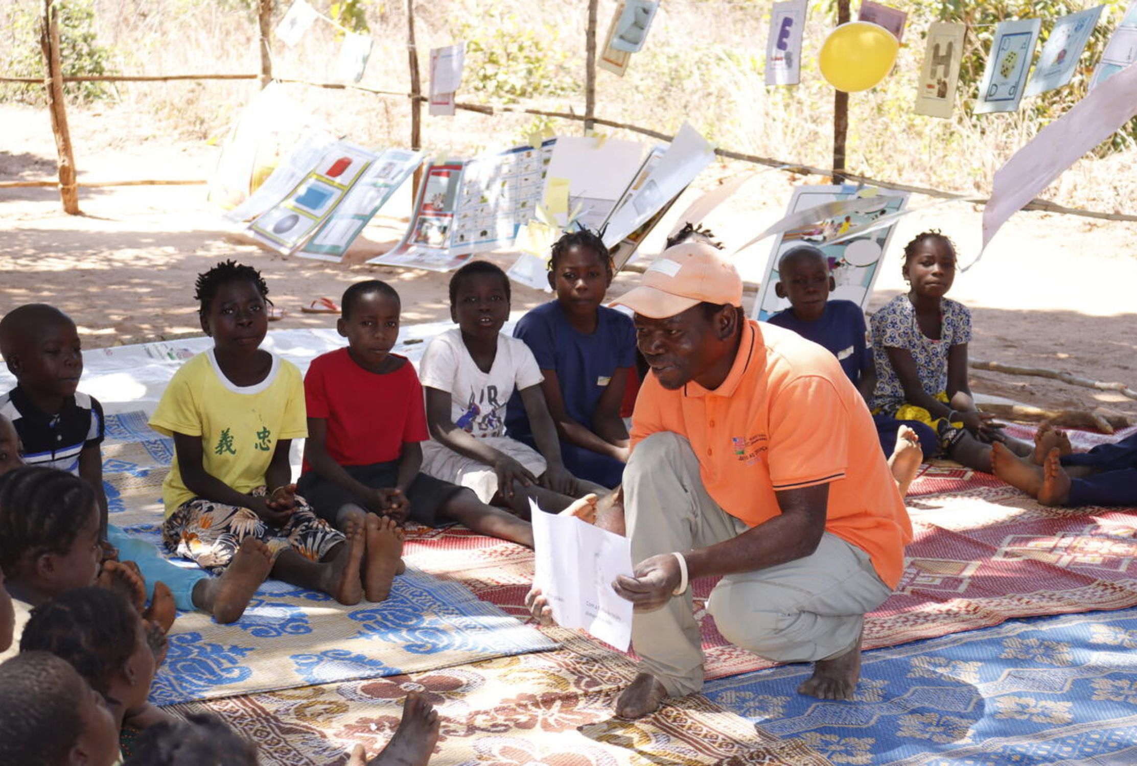 Group of children sit on the floor and learn from a World Vision a reading camp promoter