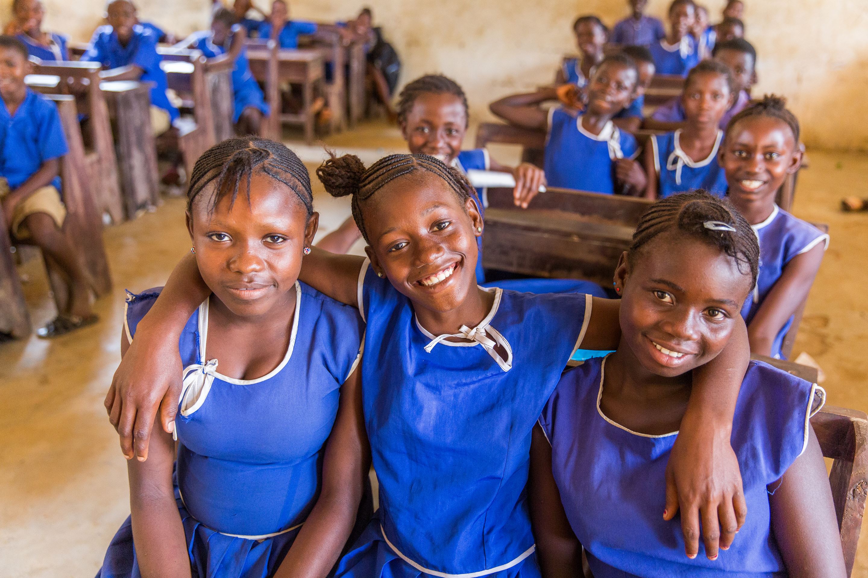 Children wearing blue school uniforms sitting in their classroom from Sierra Leone smiling to the camera