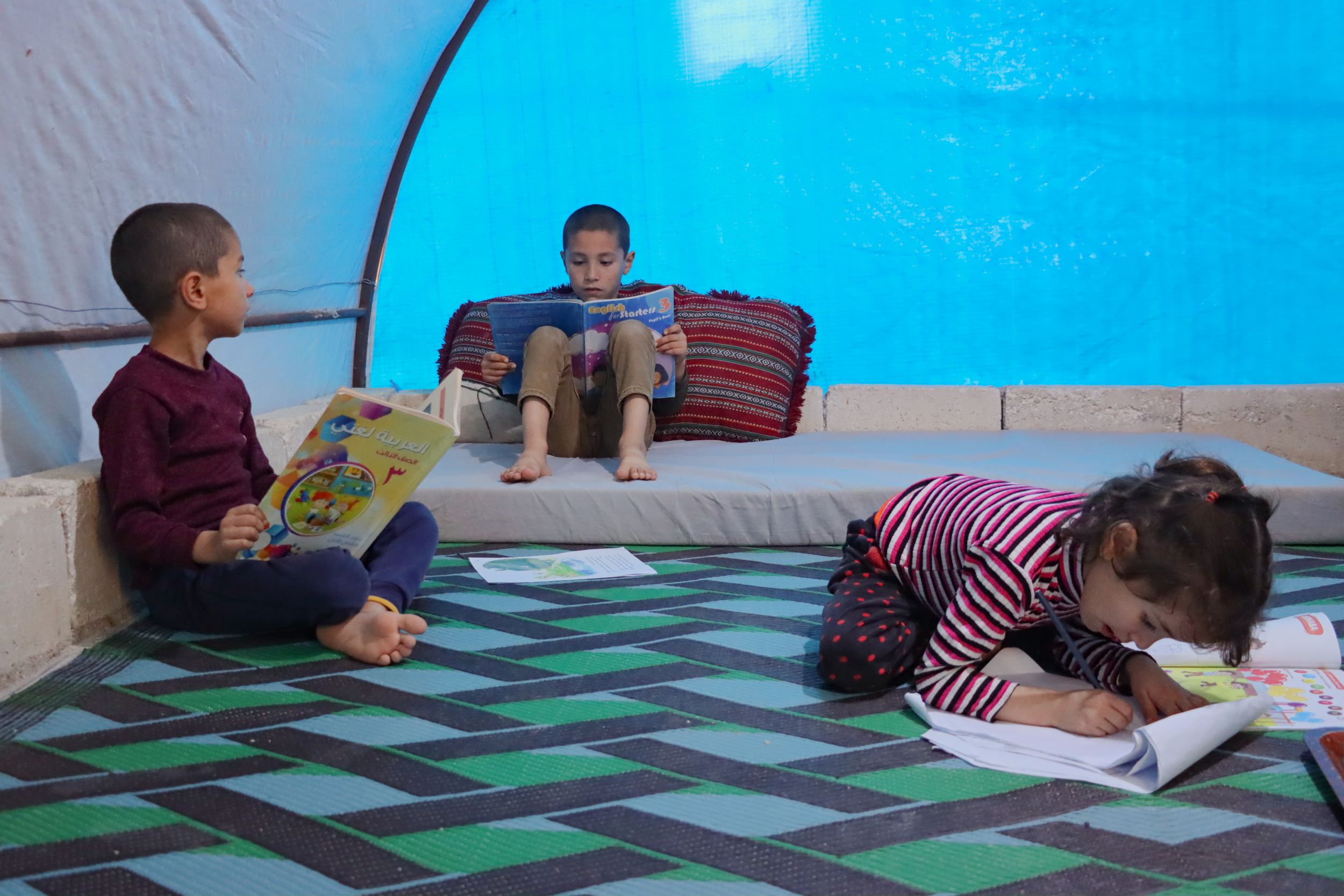 Three siblings play and read inside their tent