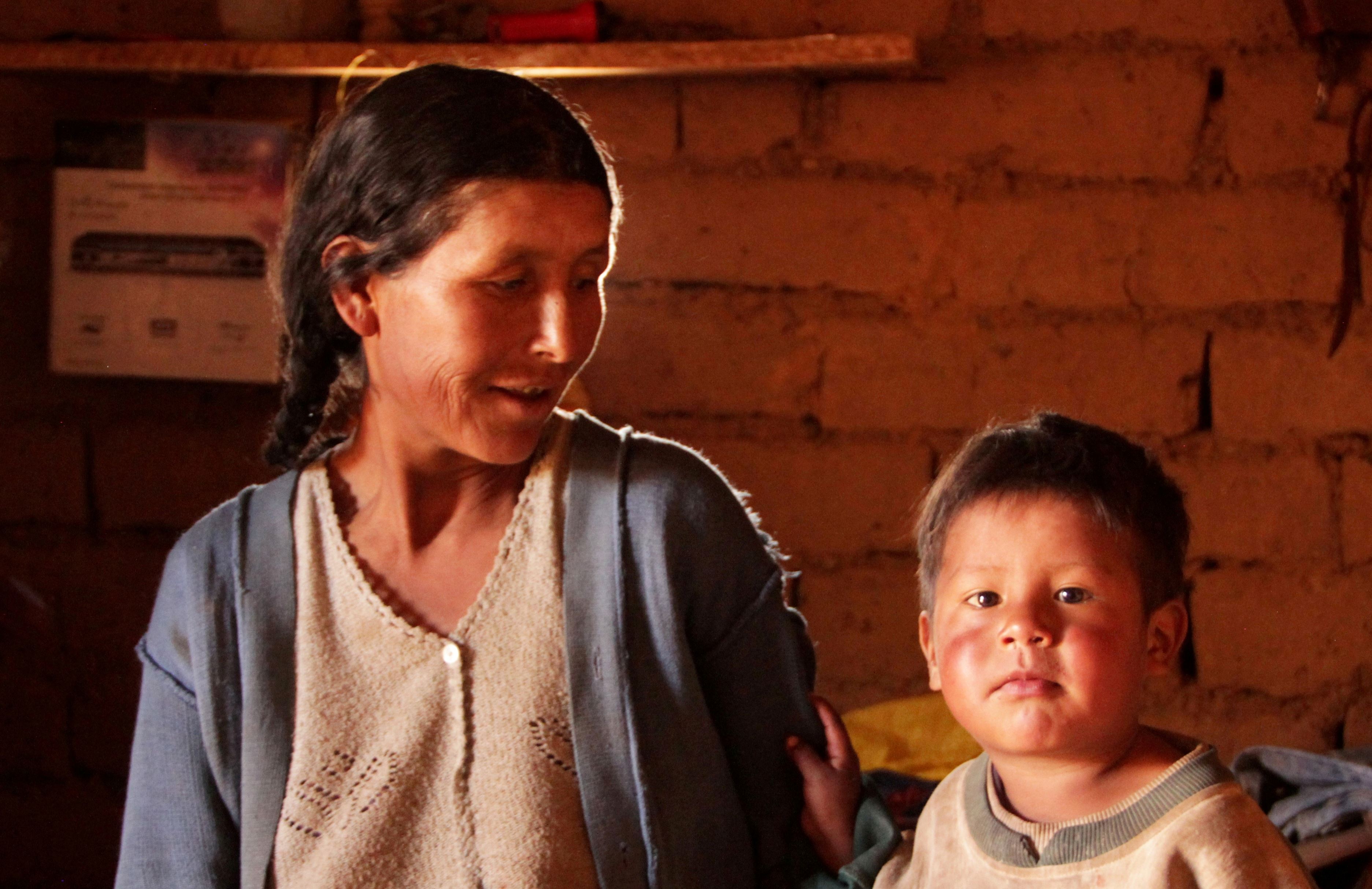 Mother and song from Bolivia with a brick background. Mother is looking at her son as he looks at the camera.