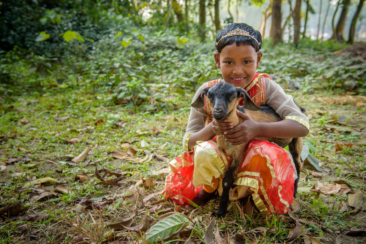 Young girl in Bangladesh hugs goat sitting in a forest