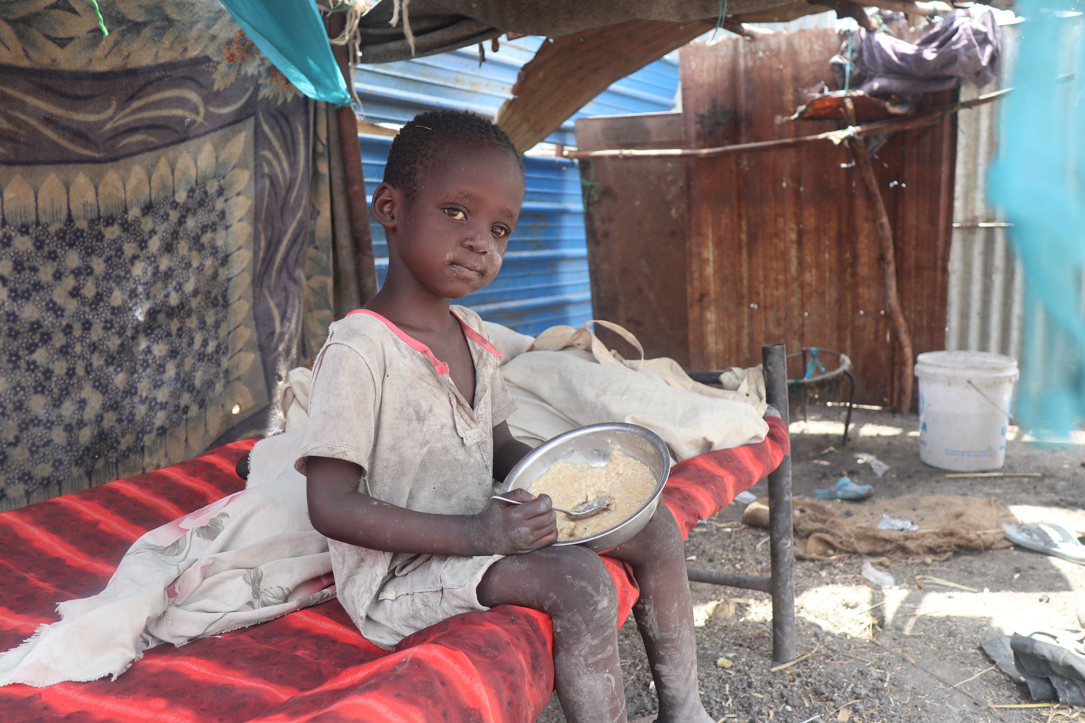 A child in South Sudan eating in a shelter at a refugee camp.