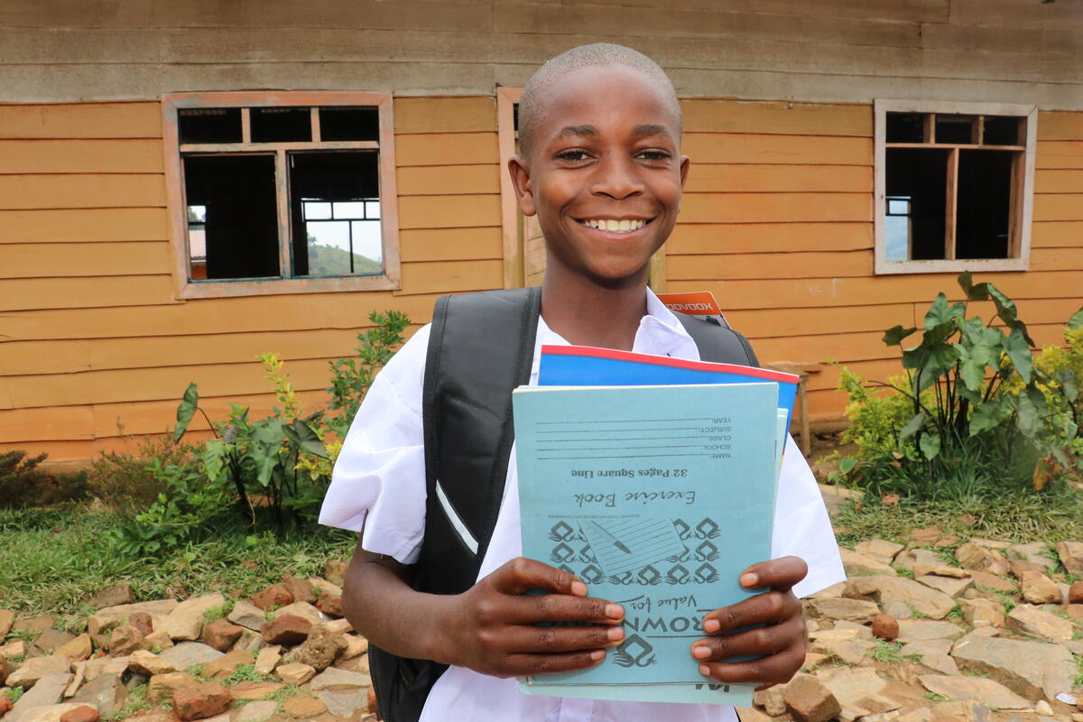 Fiston, from DRC, smiles to camera while holding his school books