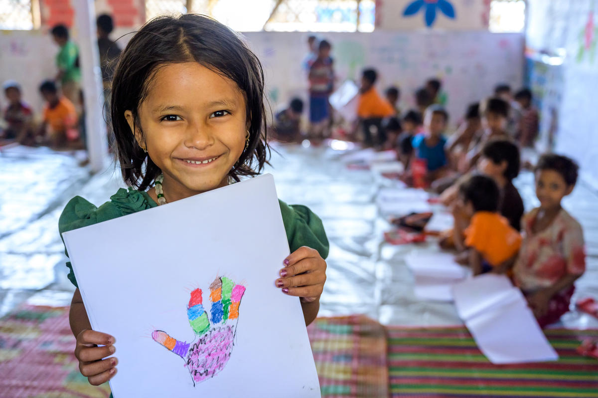 A young refugee girl in Bangladesh shows off her drawing in a class 