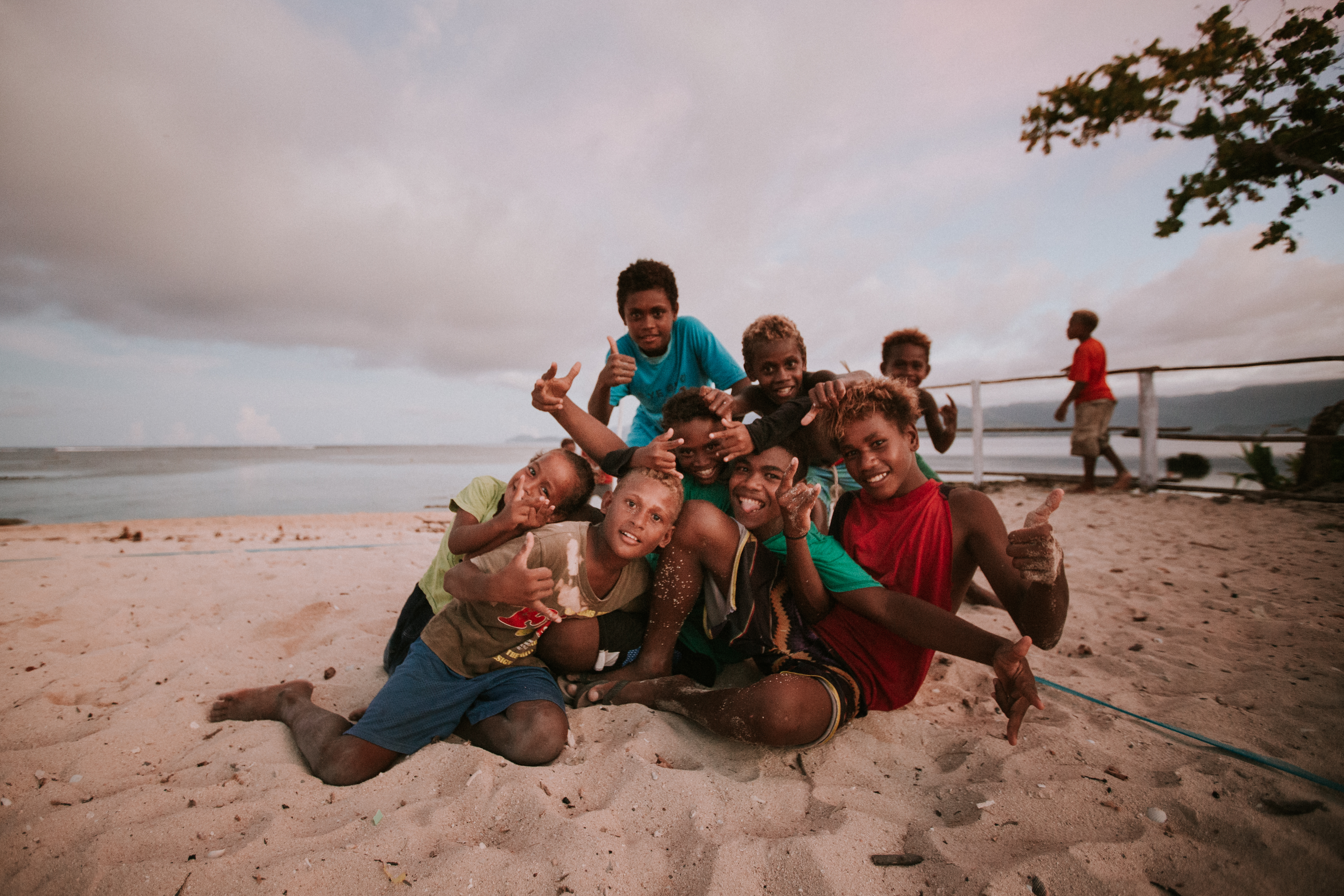 A group of boys sit together on the white sandy beach