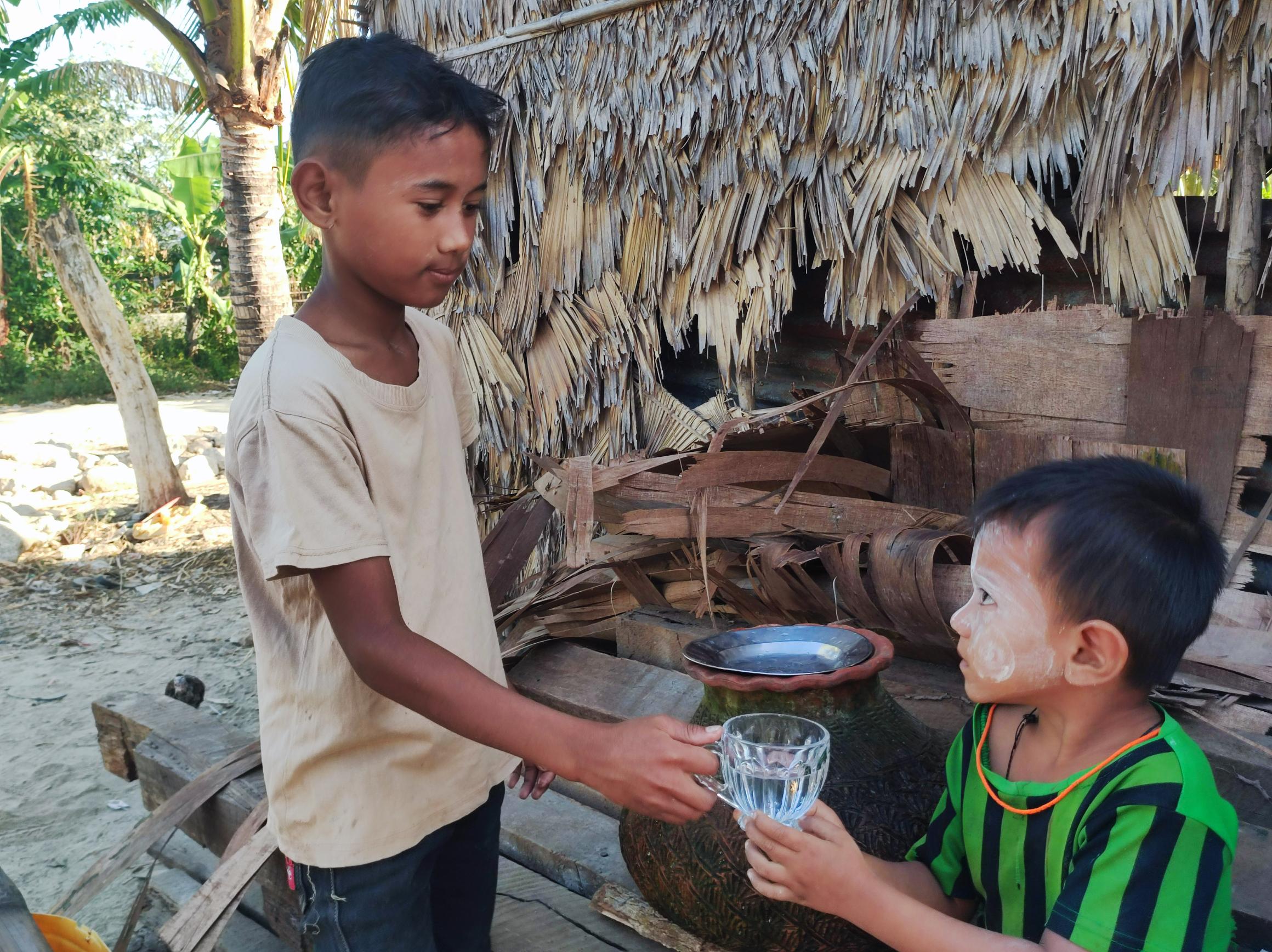 A boy from Myanmar passes a younger boy a glass of water