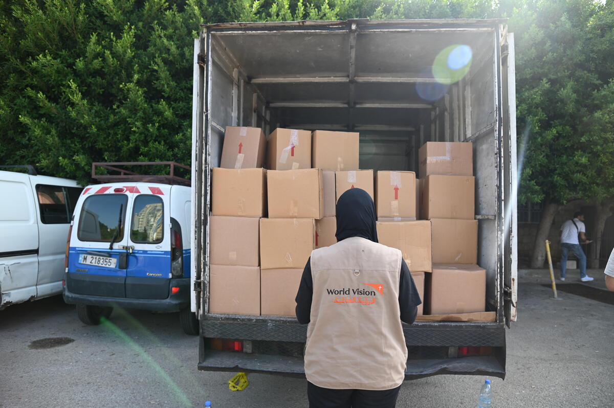 A World Vision staff faces a truck filled with essential supply boxes