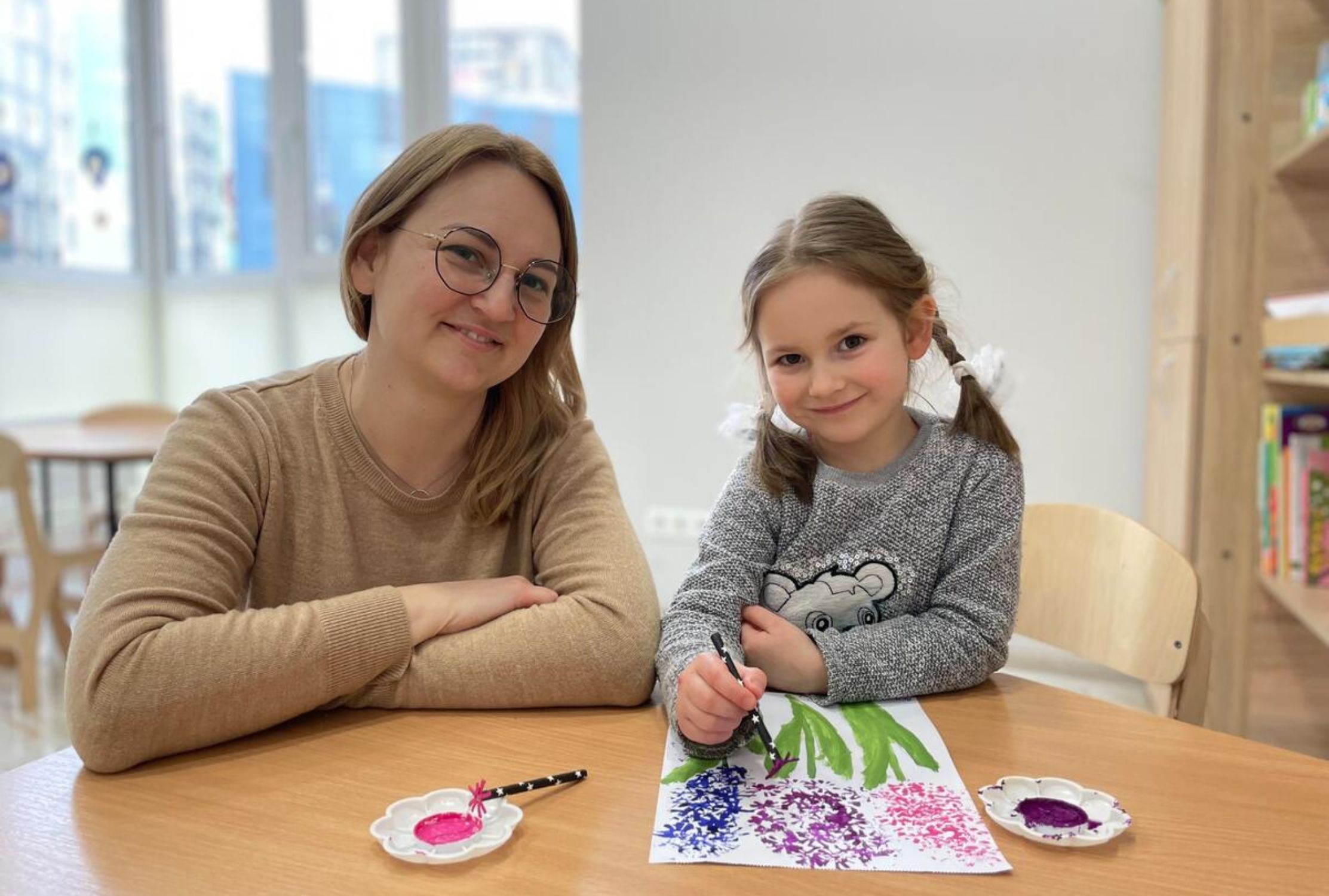 Displaced Ukrainian mother and daughter sit at a table smiling while doing a flower painting