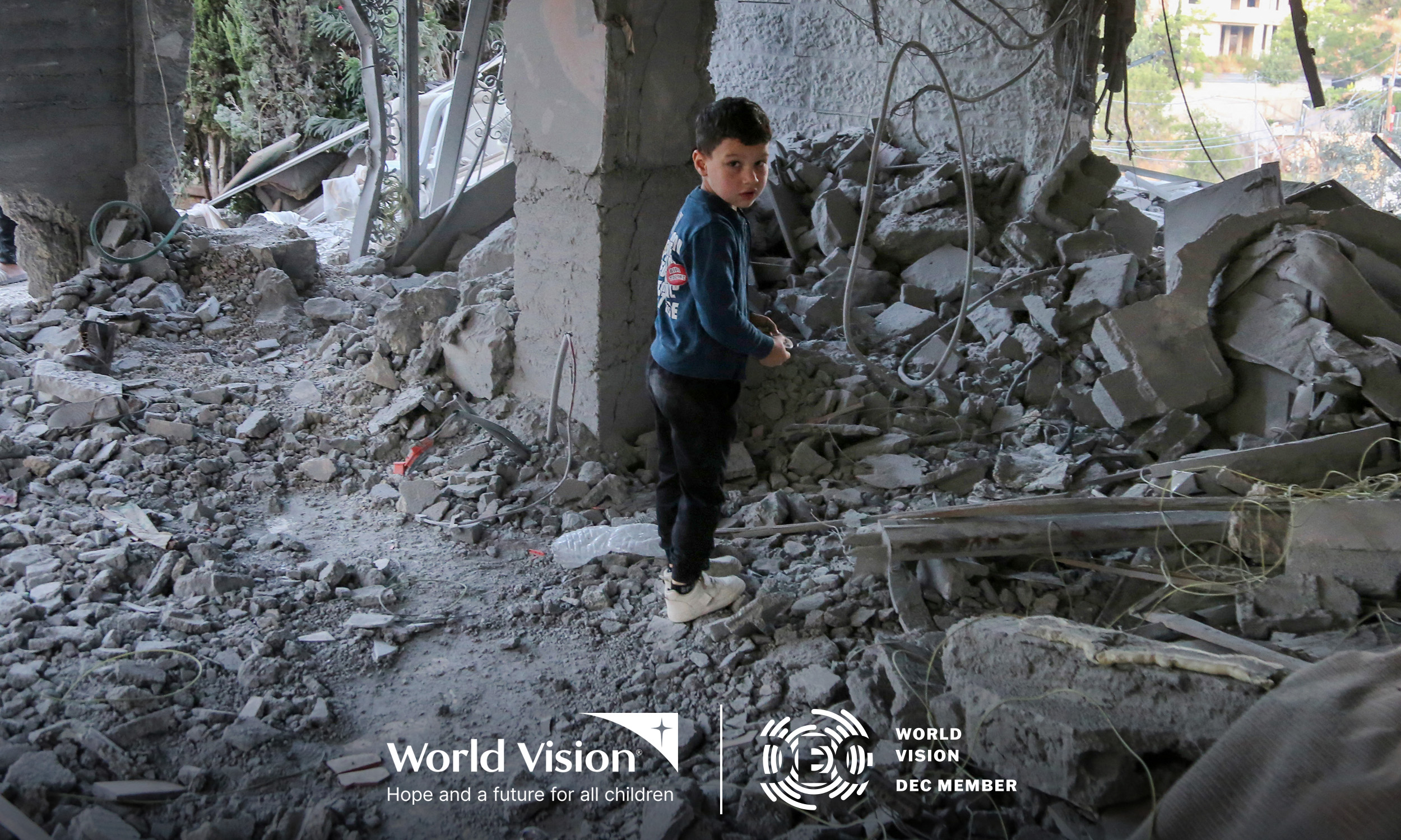 A young boy stands amidst the rubble of a building