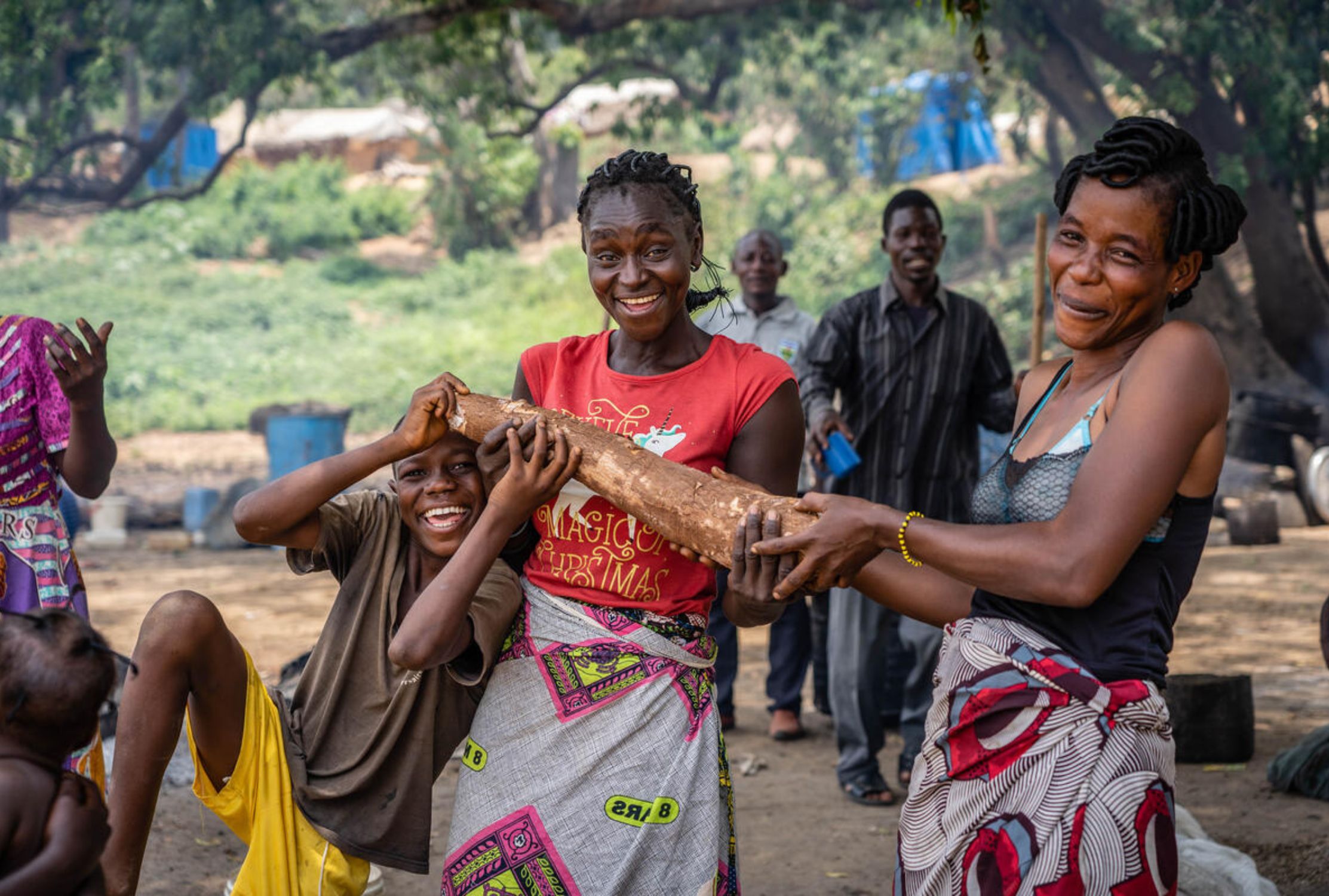 Two women and a young boy playing and laugh while holding a small wooden log.