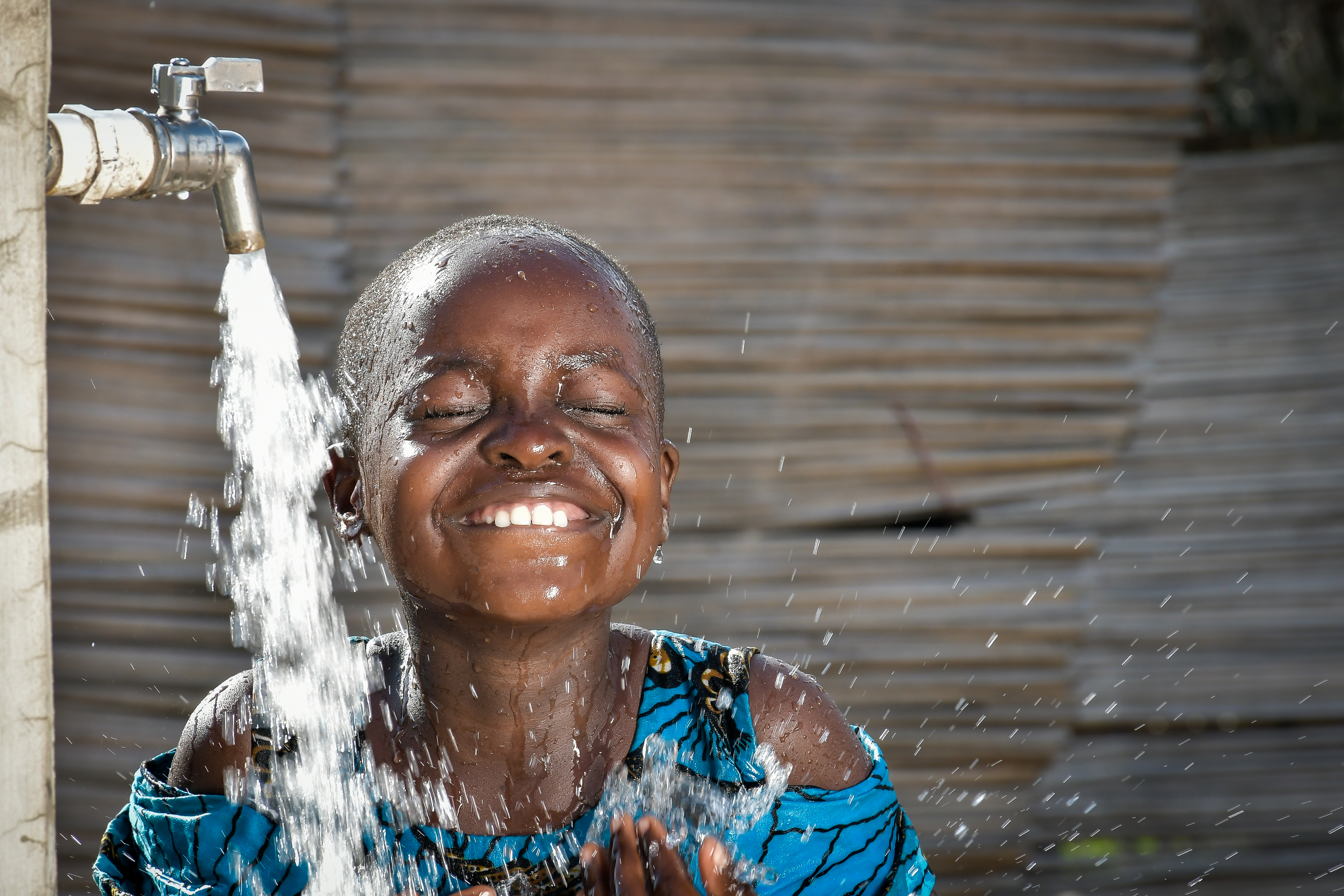 A girl in Ghana smiles as she splashes under a running tap