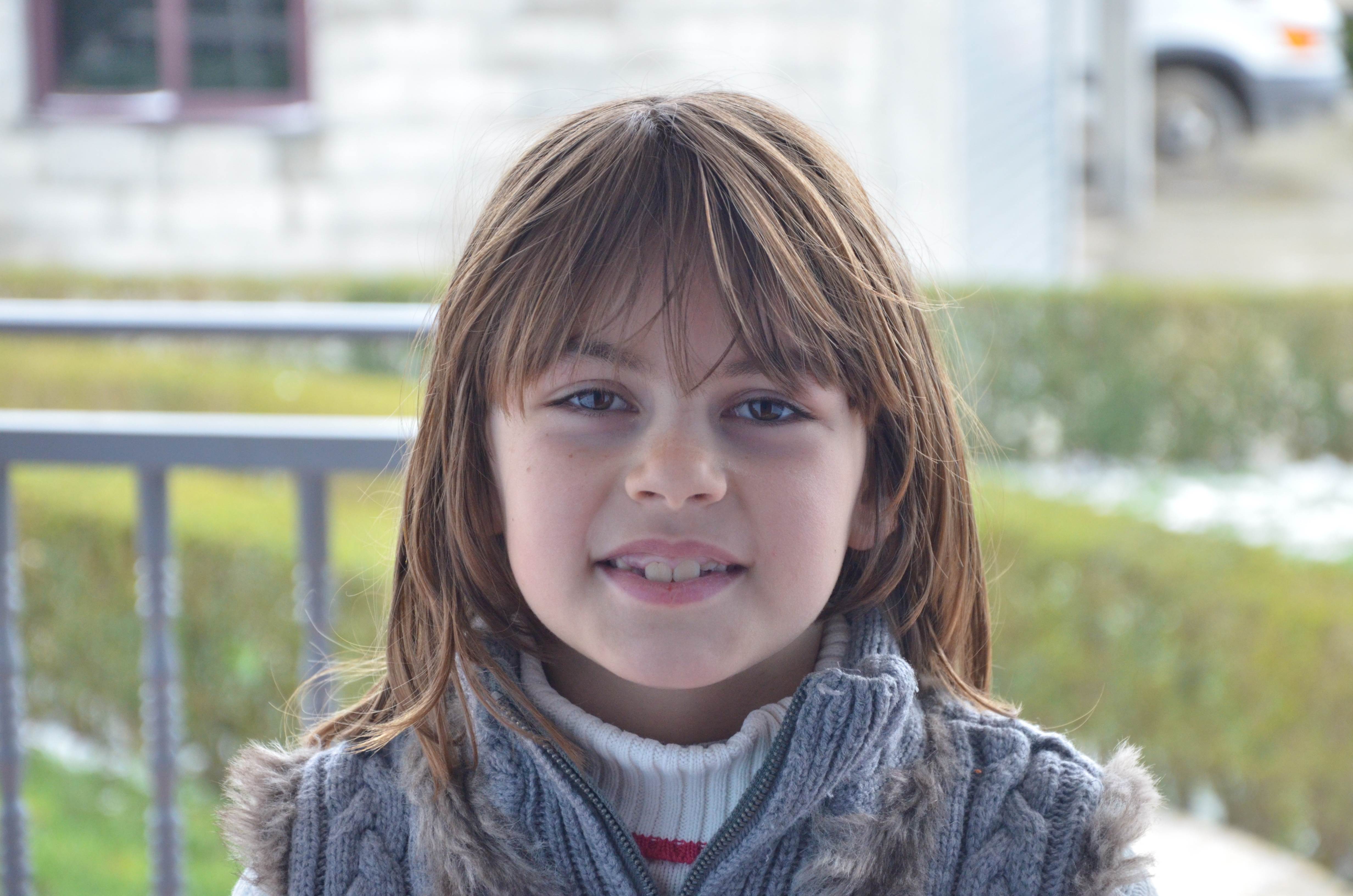 Girl smiles at a camera wearing a warm jacket against the backdrop of her neigbourhood in Albania