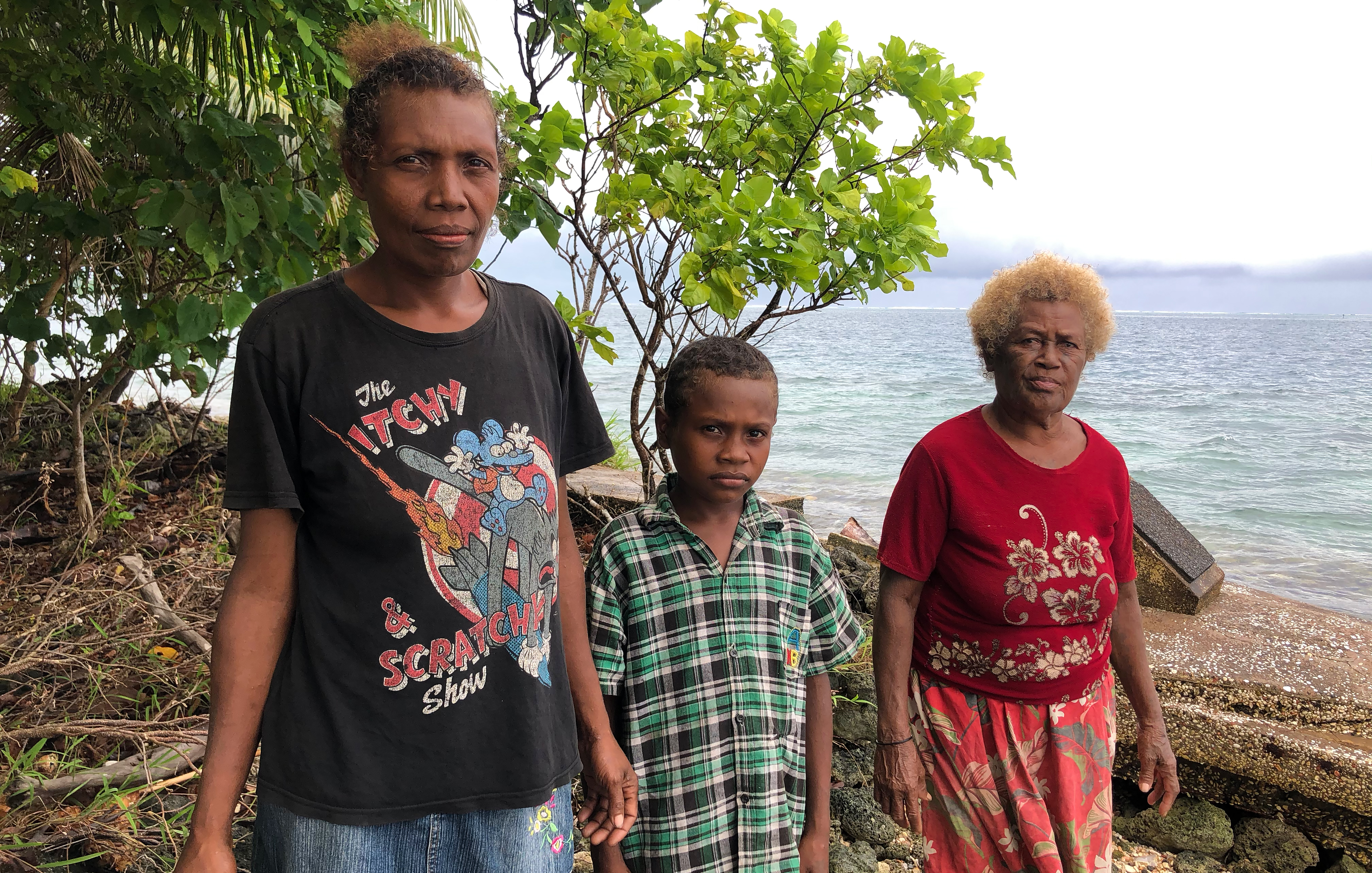 Three generations of a family stand on the island in Solomon Islands that would have been their home were it not for climate change