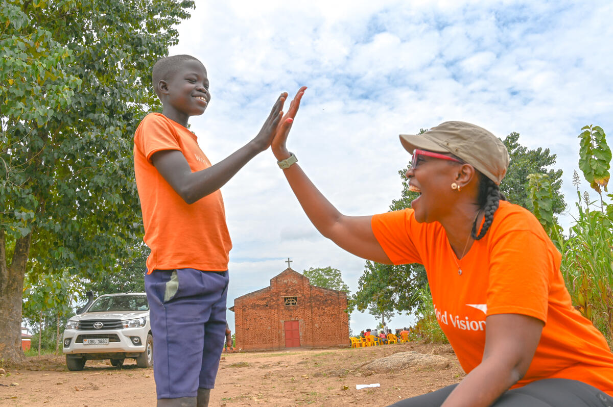 Isaac, a young boy from Uganda, shares a high five with Helena, a World Vision staff memberg smile on his face alongside a World Vision staff member