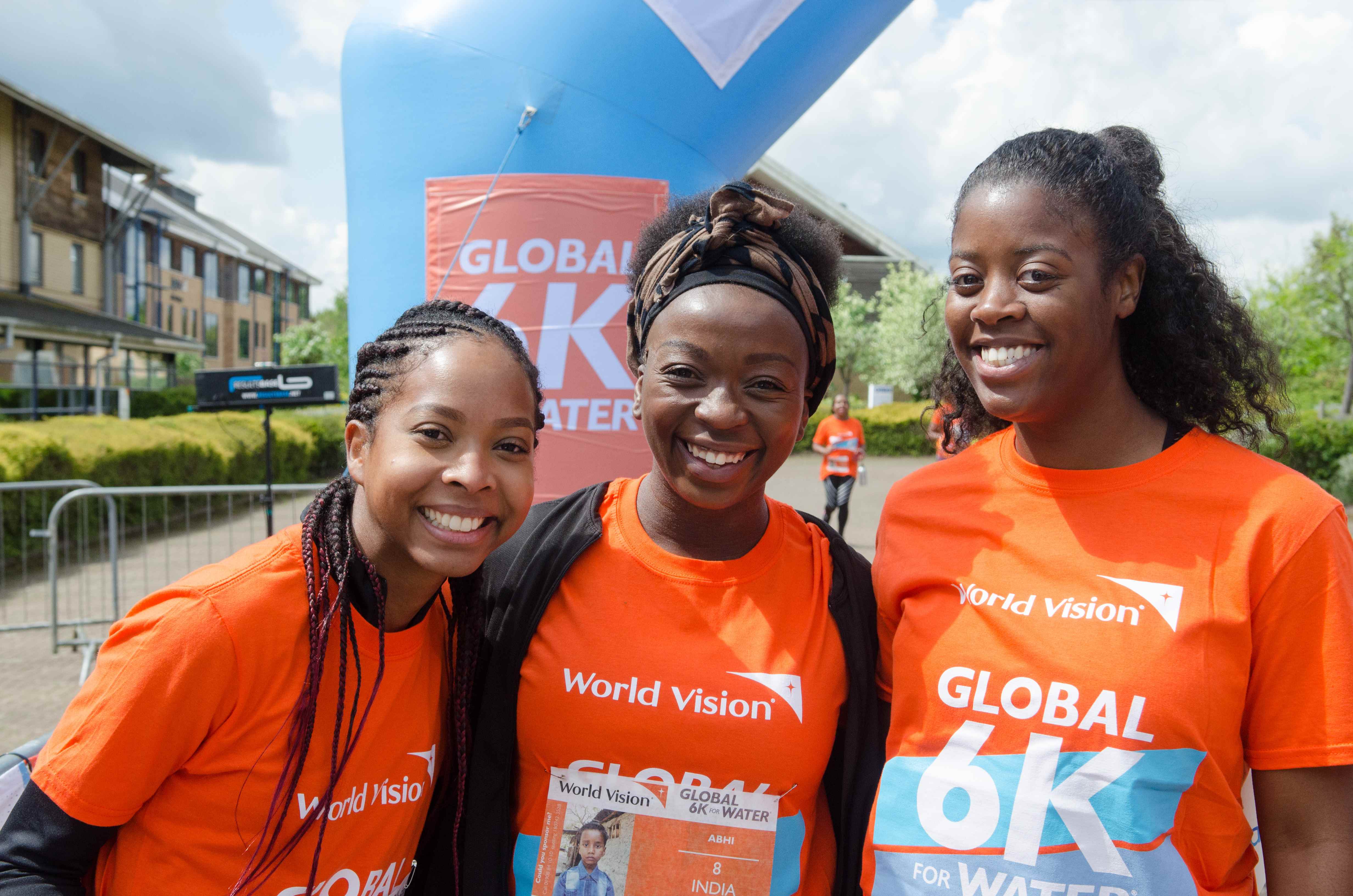3 people in orange World Vision t-shirts smiling to the camera at a Global 6K event