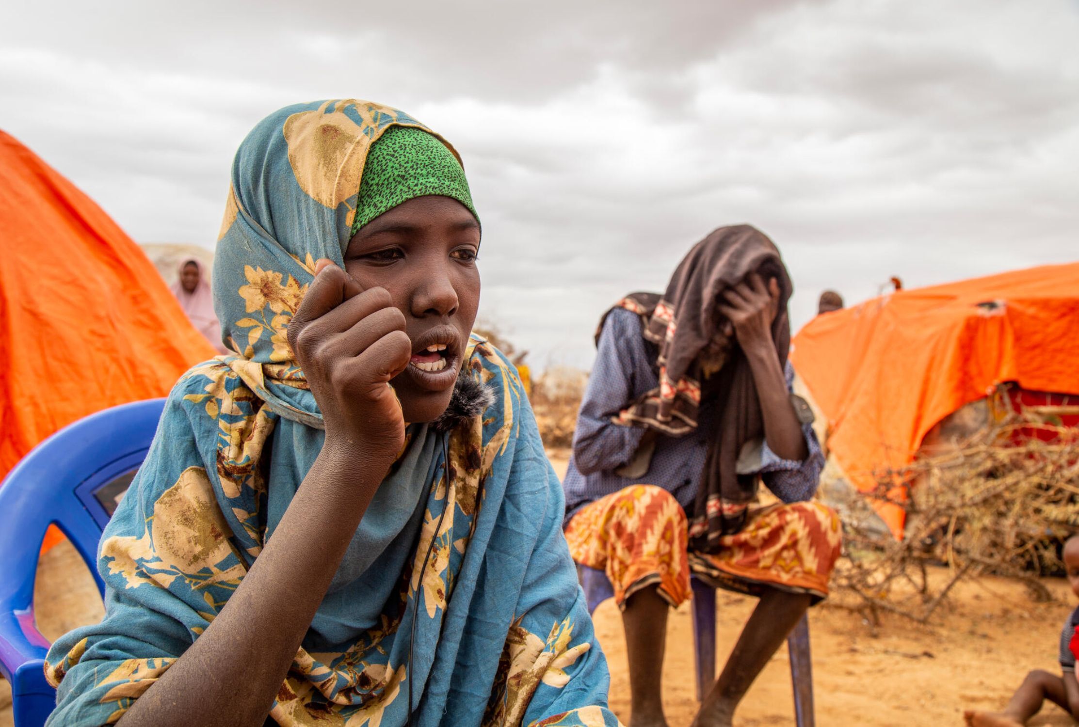 Somali girl wearing a hijab sat outside makeshift home with her blind father.