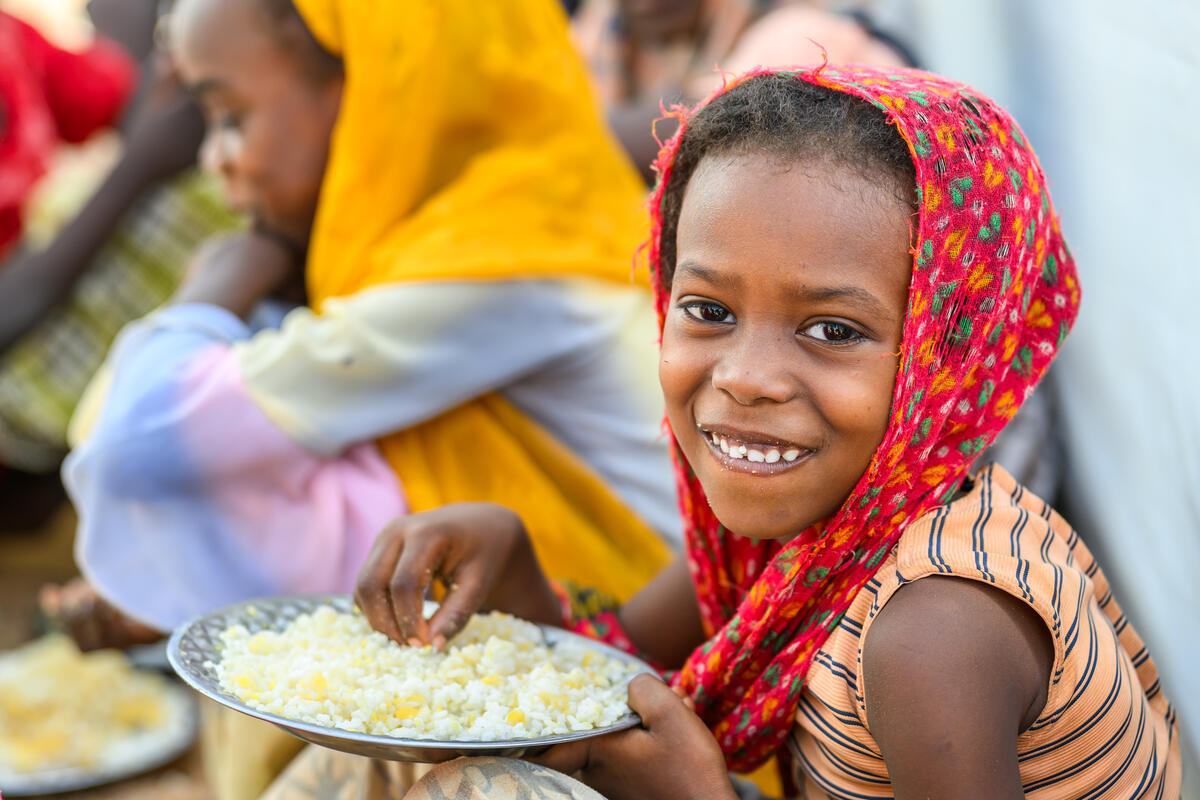 A refugee child with a plate of food smiles at the camera, Chad