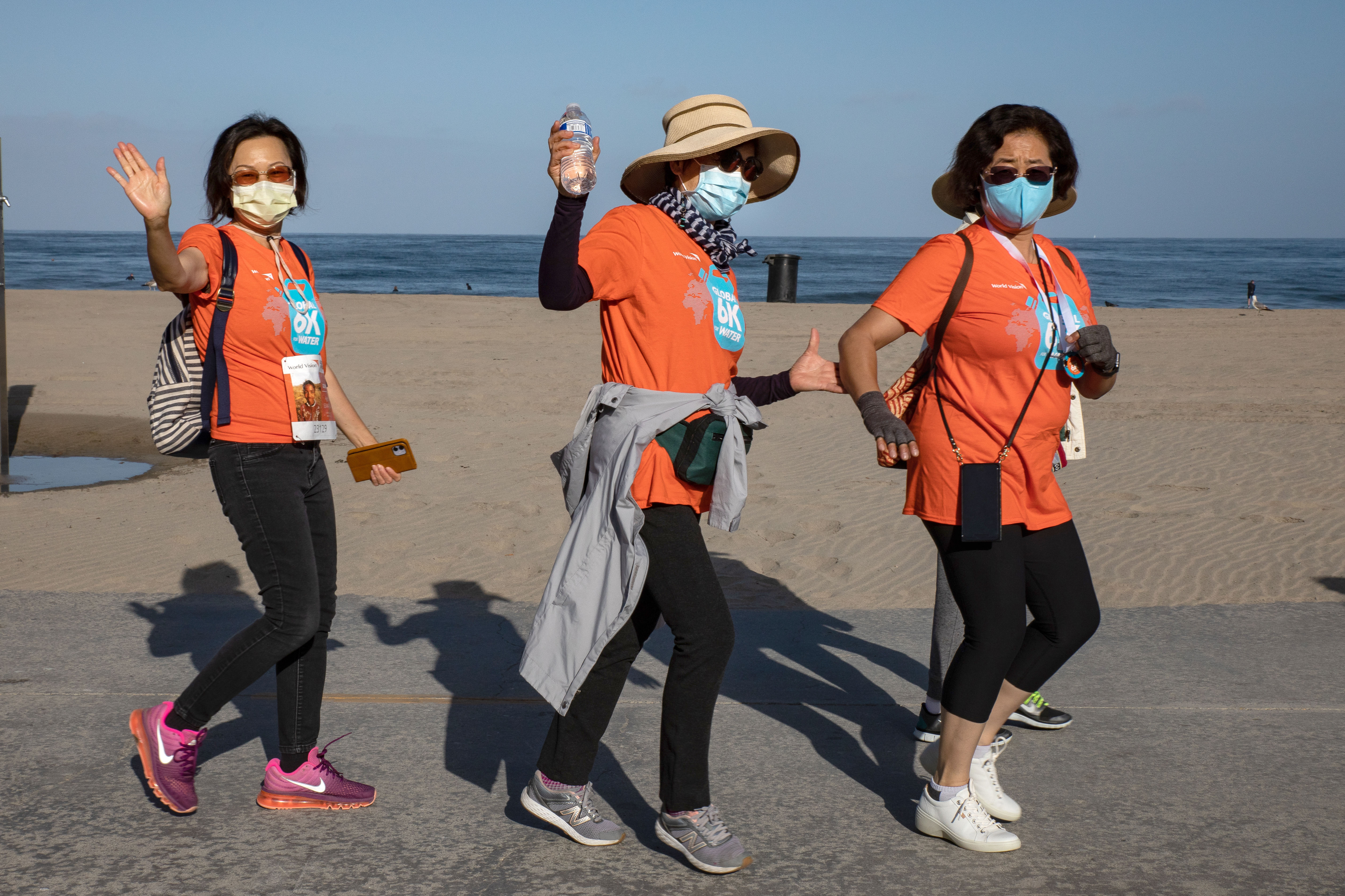 Three women in orange t-shirts walk along the beach front together