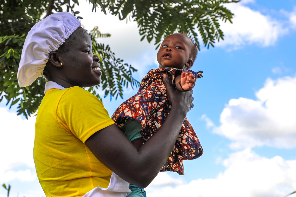 A Ugandan mother holds up her baby girl, blue sky in the background