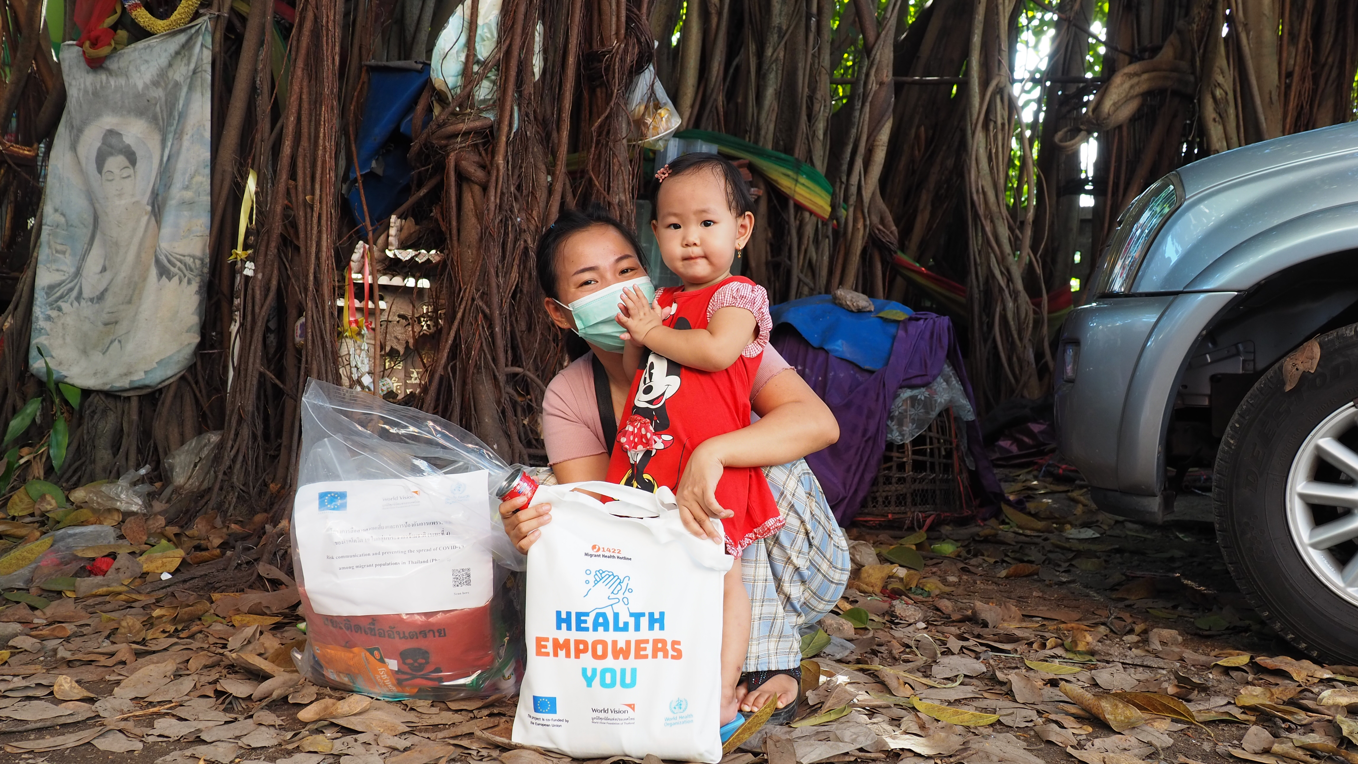 A woman from Myanmar wearing a surgical face mask pictured with her toddler daughter. The woman is carrying a bag of emergency aid donated by World Vision