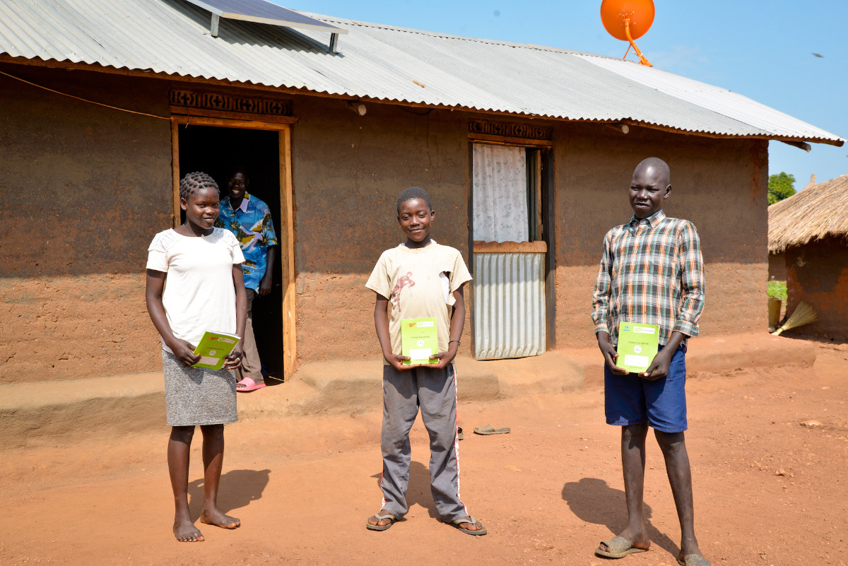 Three children stoof outside holding green books.