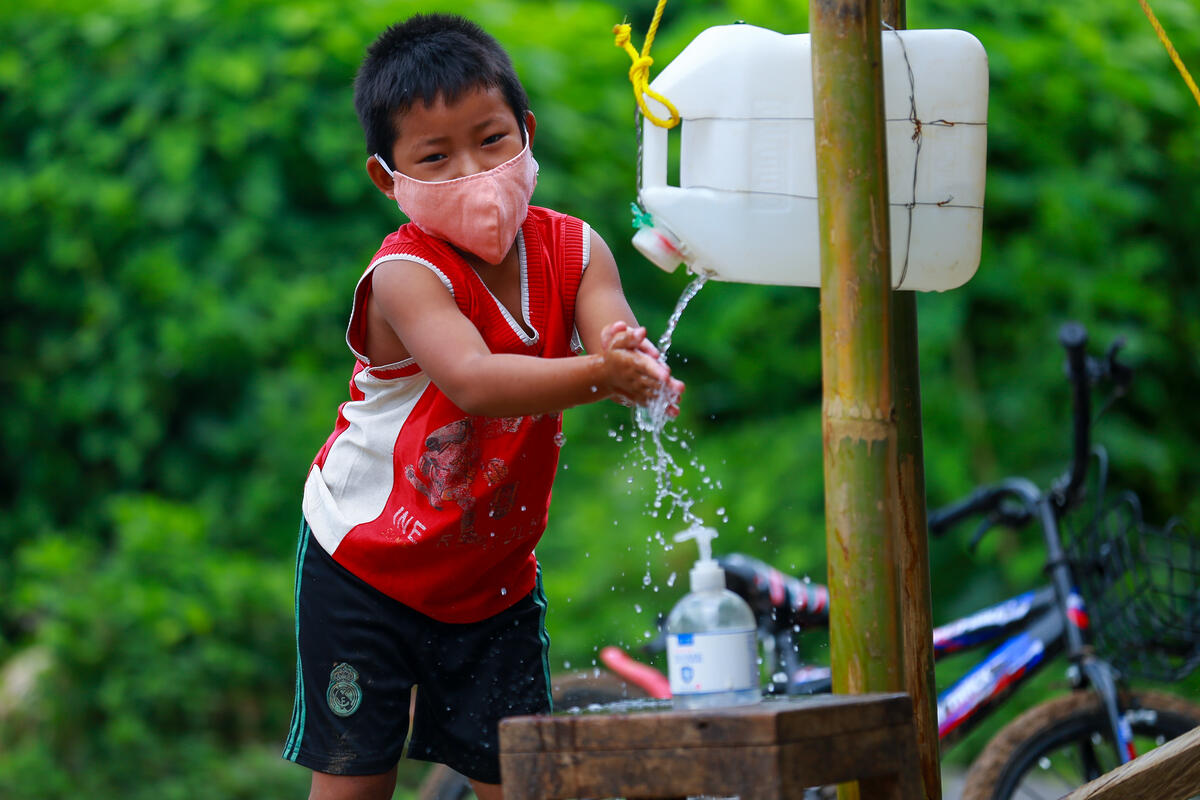 Young boy washes his hands at a makeshift tap with a mask on