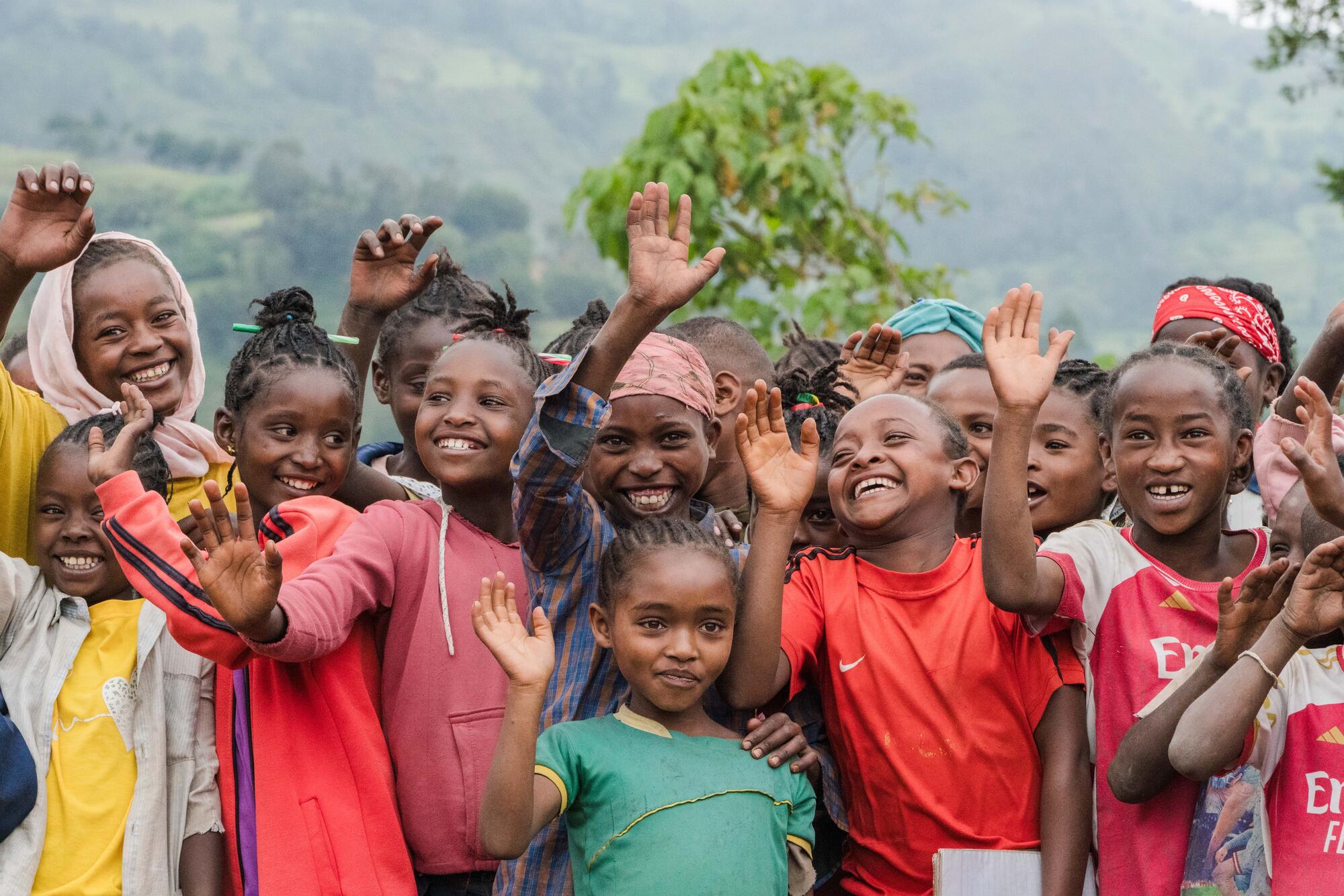 A large group of young children in Ethiopia smile and wave to the camera