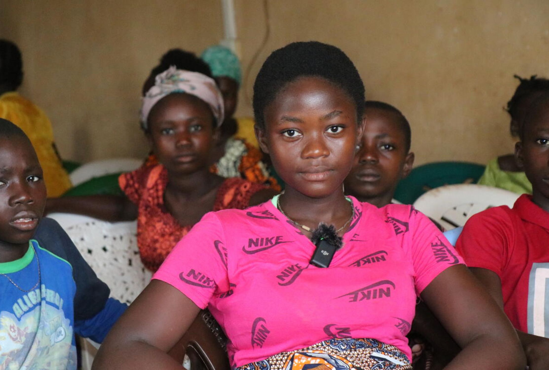 Girl wearing pink looks into camera with other children behind her