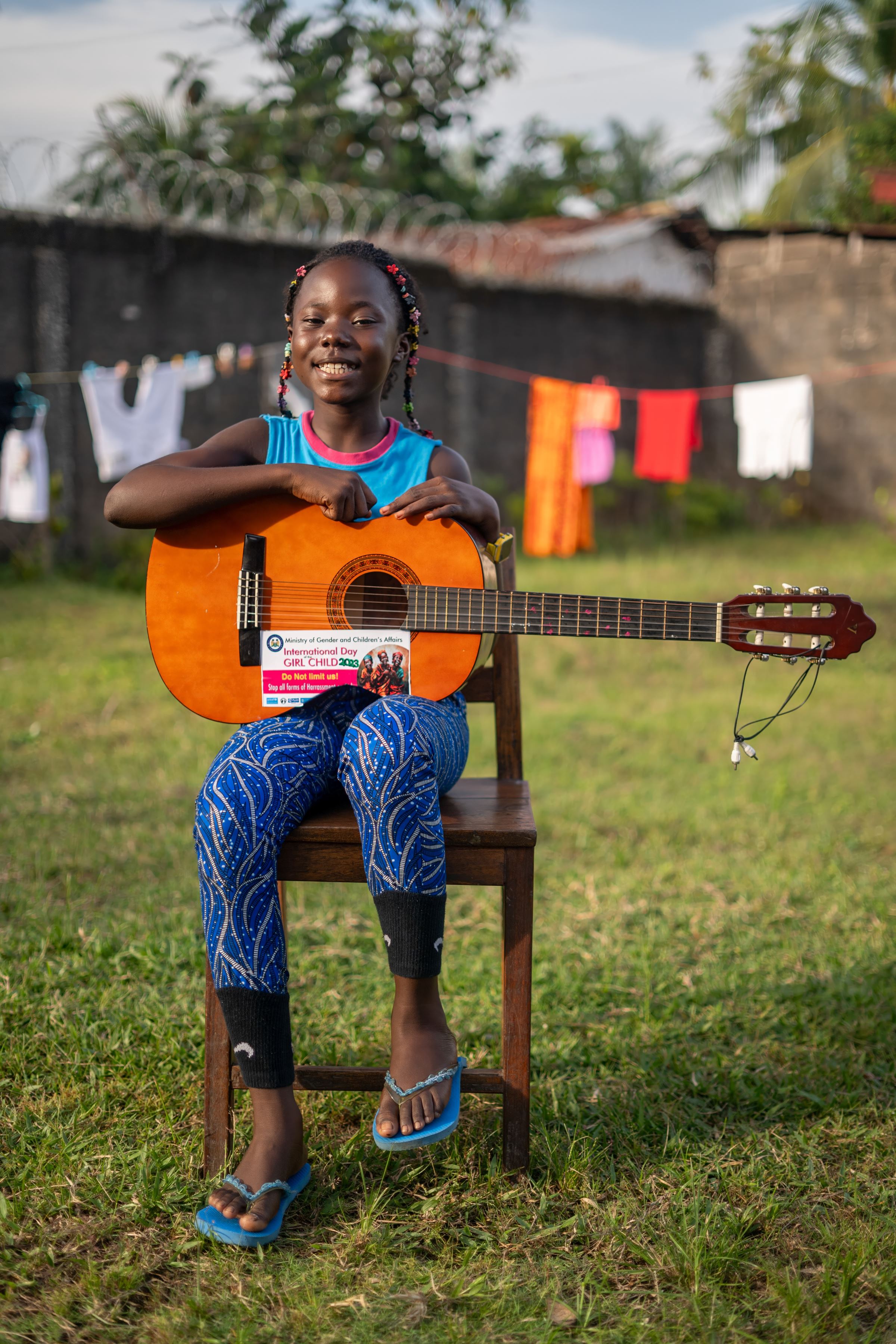 Jospehine, sits on a chair holding a guitar, smiling to camera