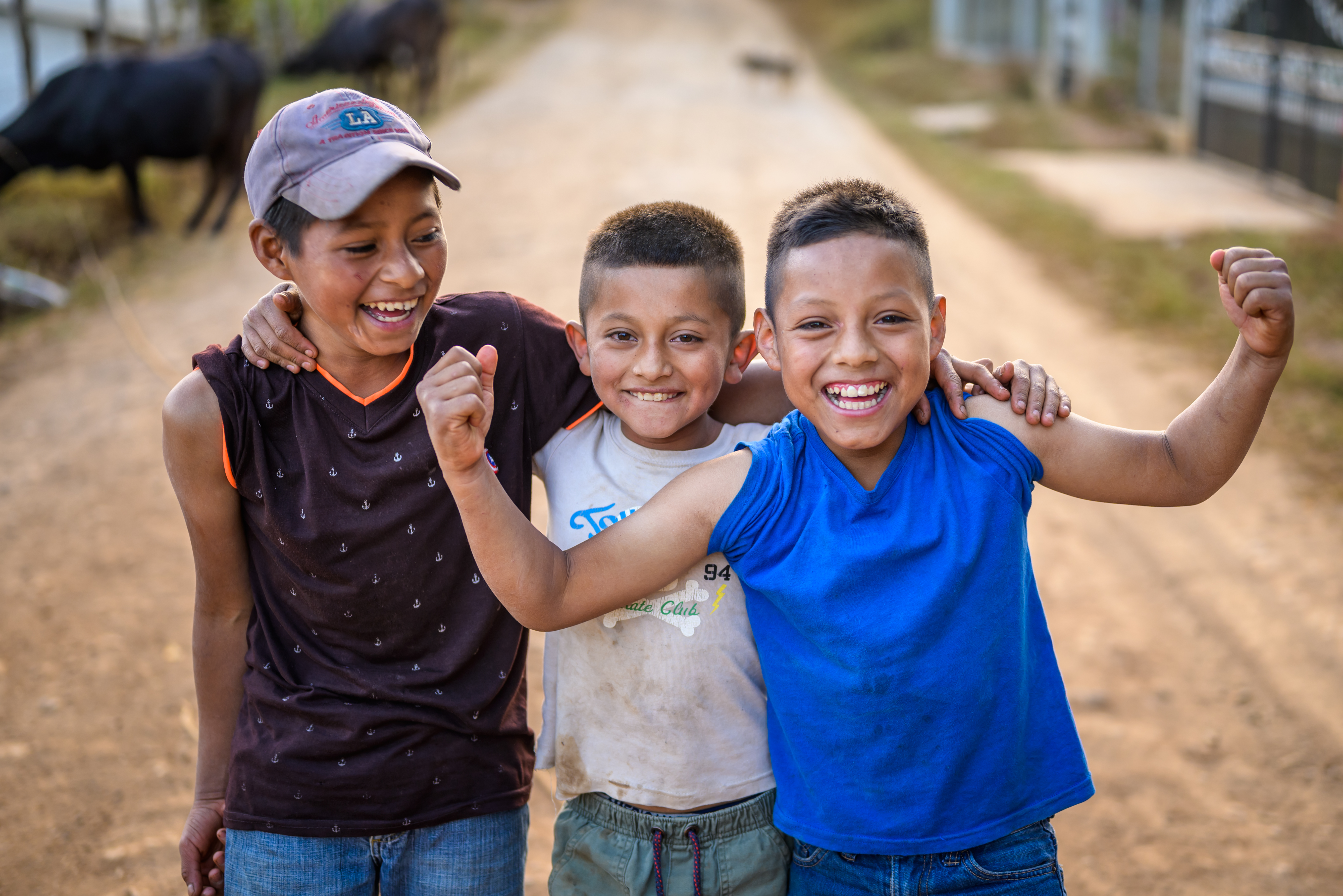 Three boys from Honduras grin and link arms and smile at the camera as one of them shows off his muscles to the camera