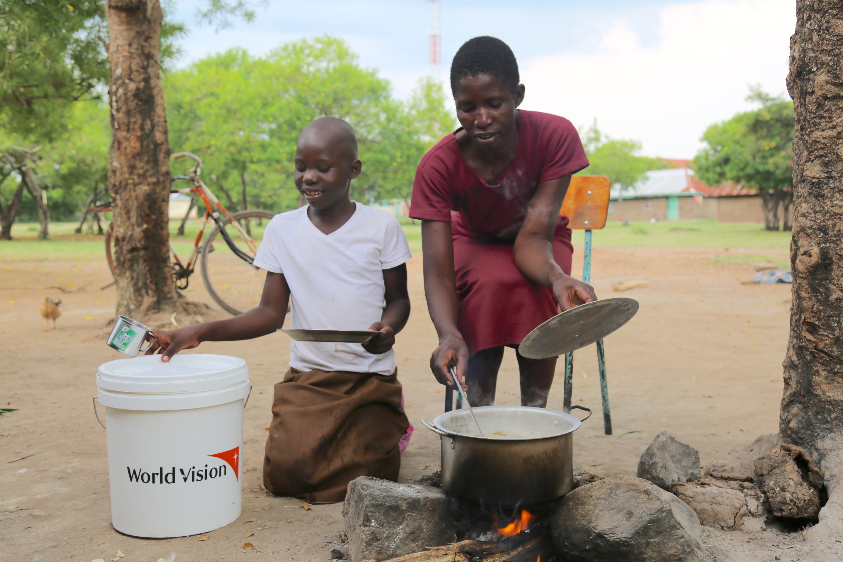Two people kneel next to a cooking pot outdoors in Kenya