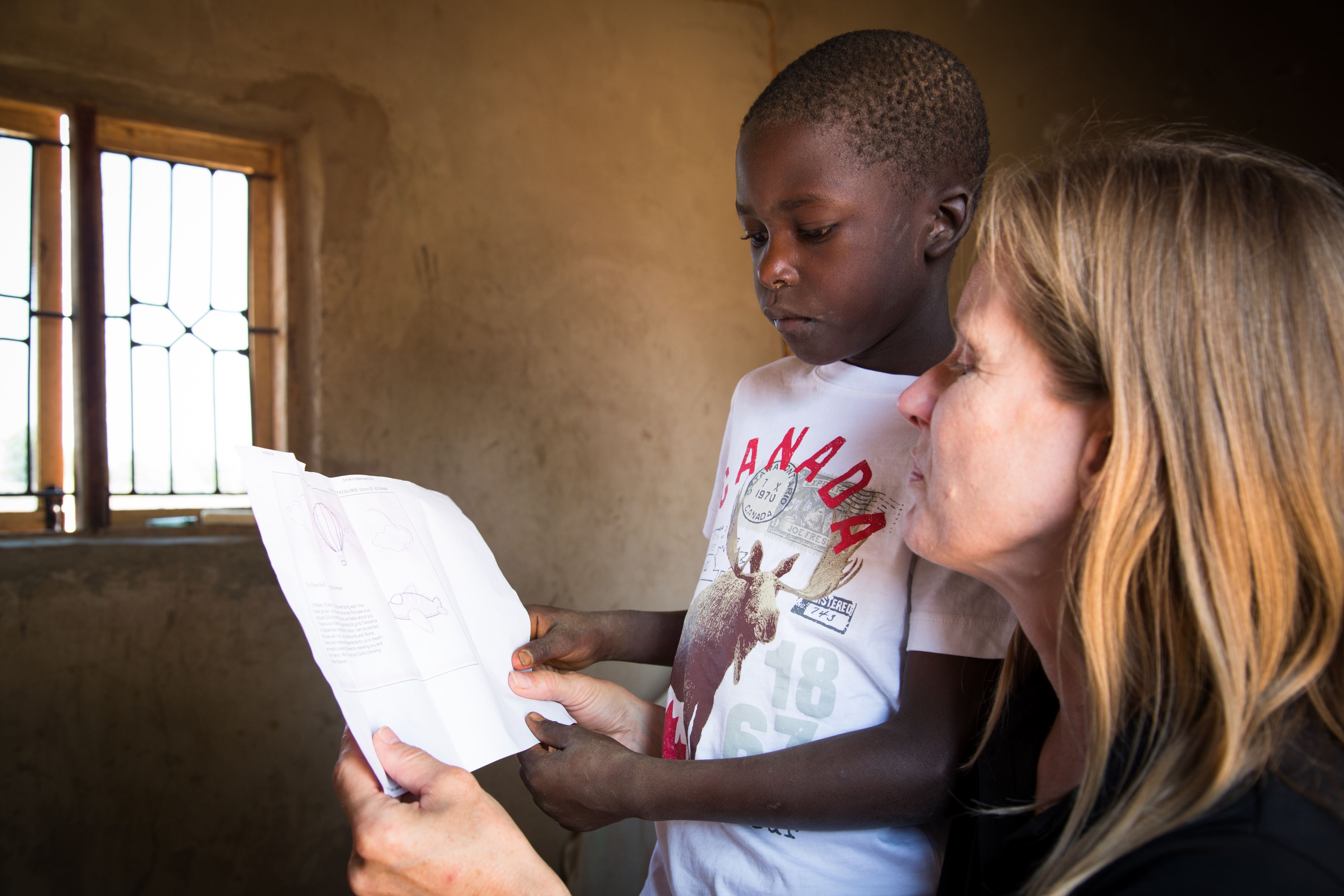 Tanzanian child reads a letter held up by an older woman